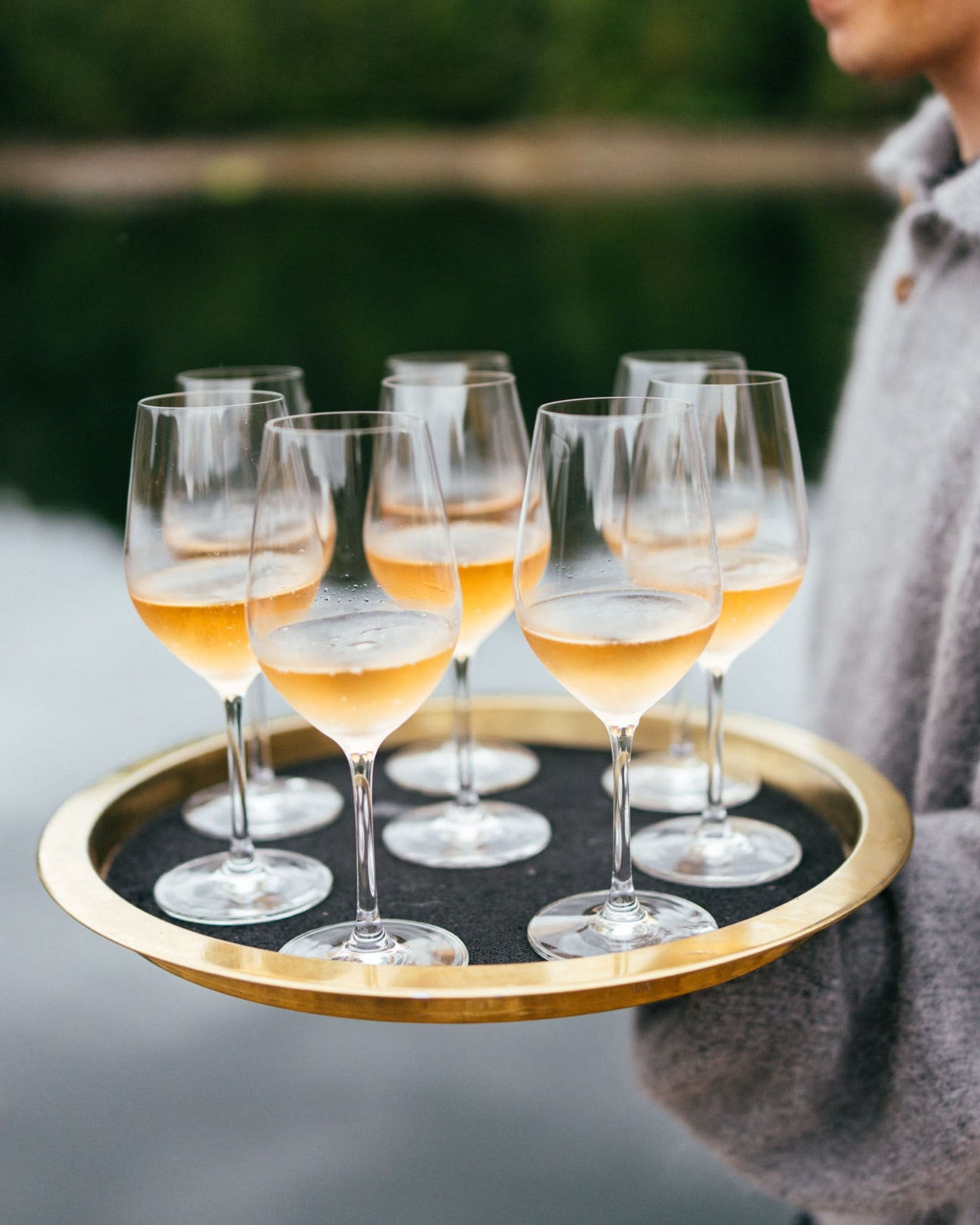 Person holding a tray with wine glasses by the ocean