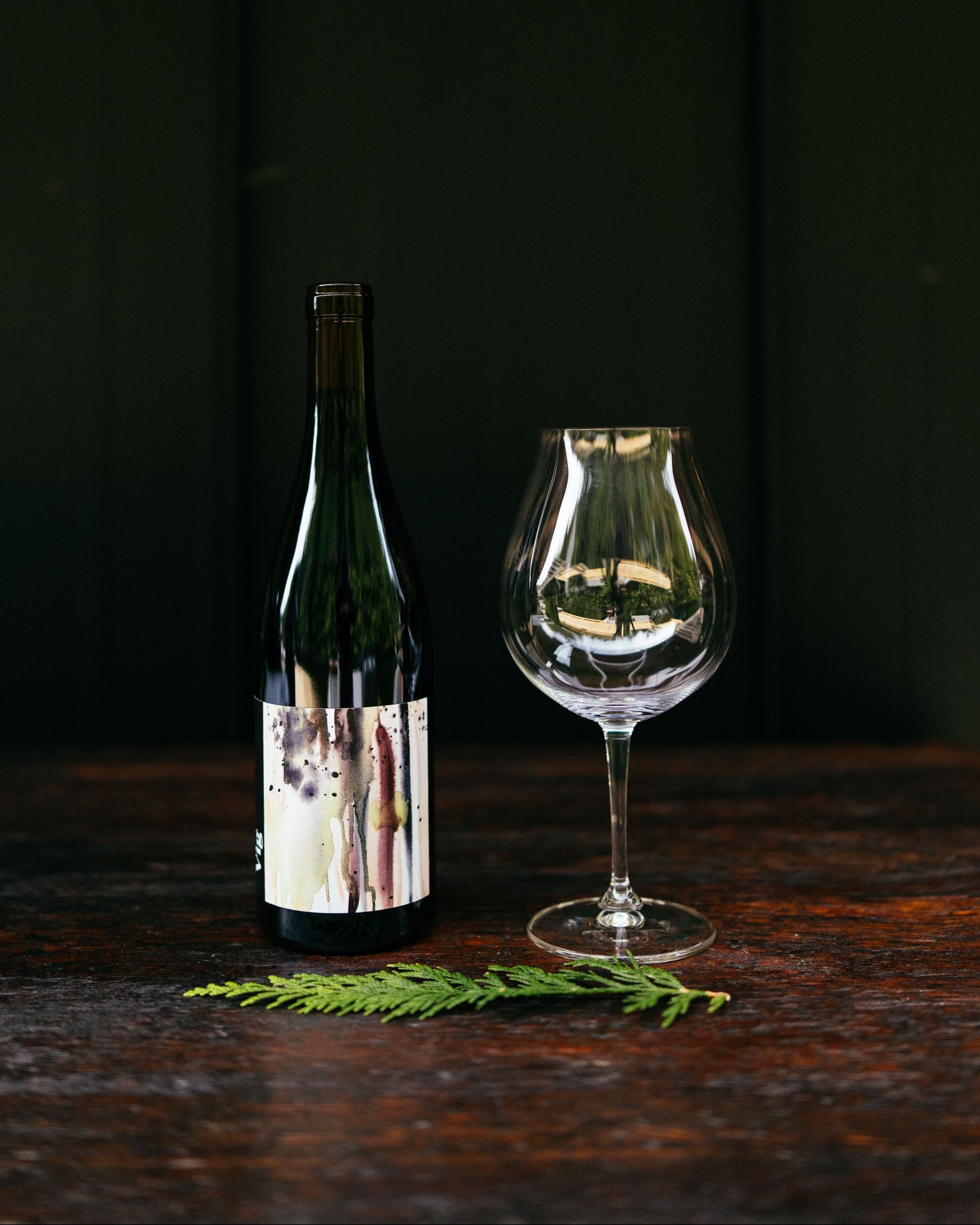Wine bottle and glass on a dark wooden surface with a dark background