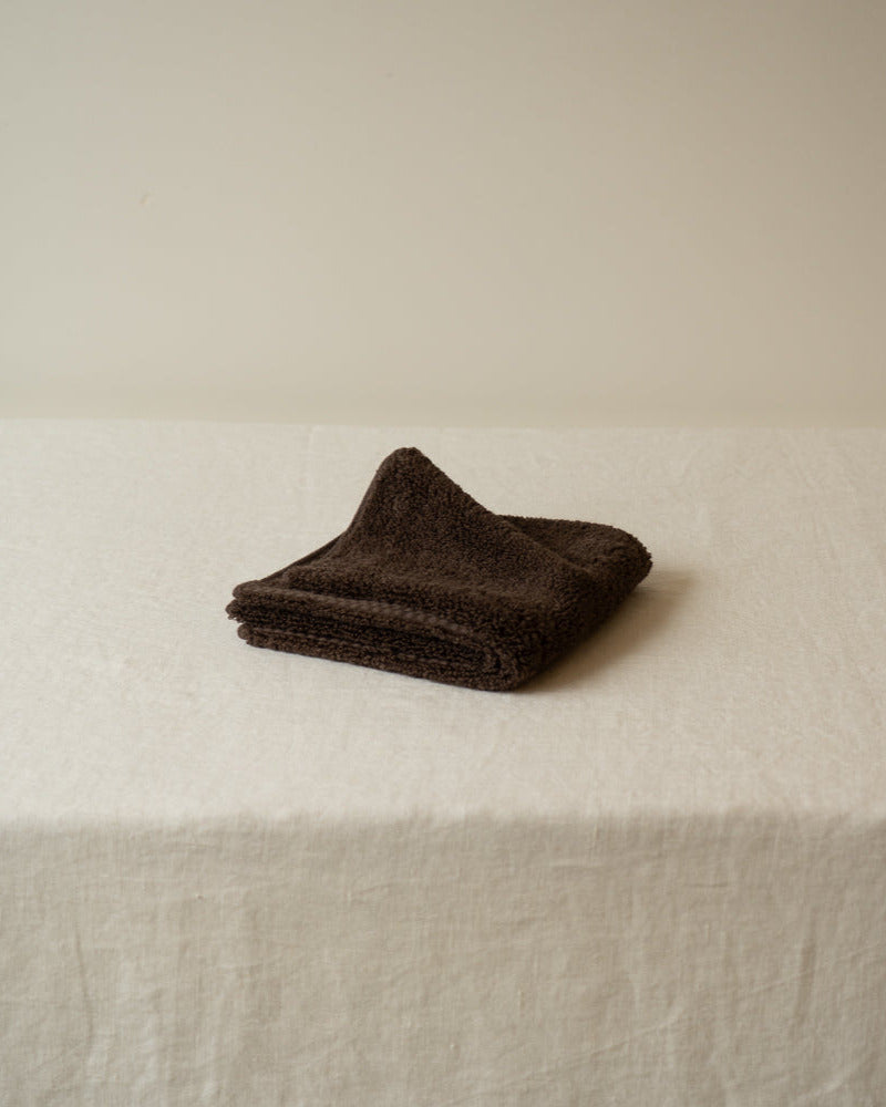 Folded brown towel on a white surface with a neutral background