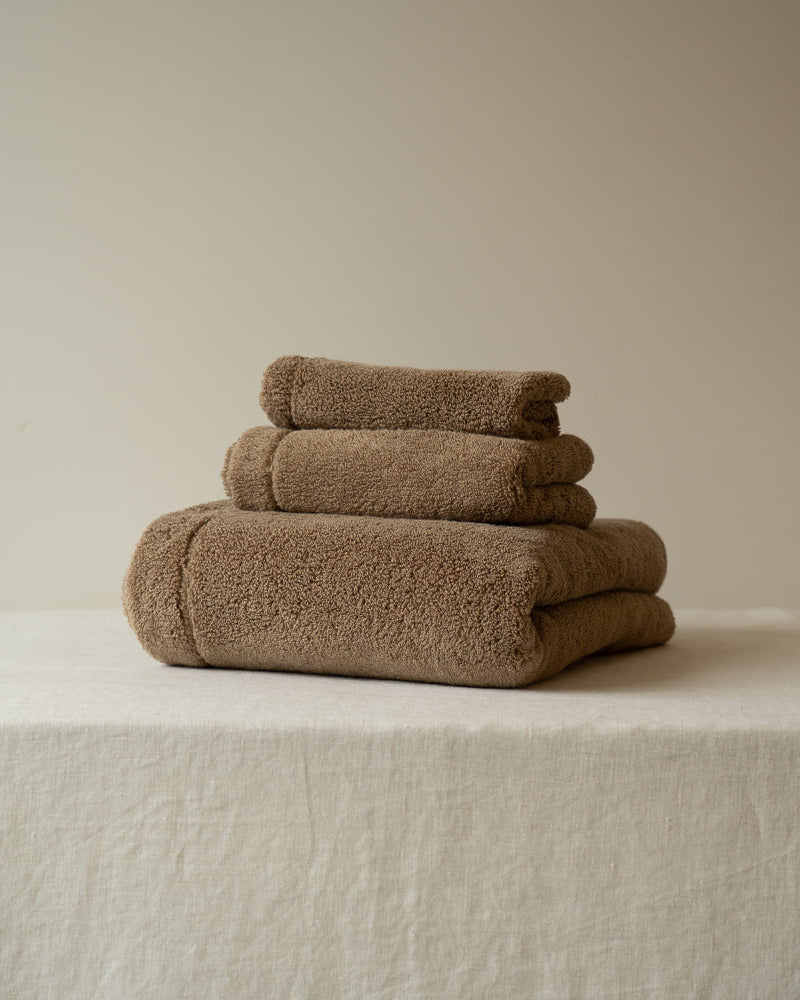Stack of brown towels on a white surface with a beige background