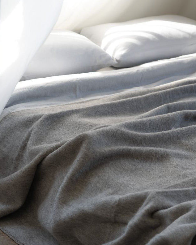 Gray blanket on a bed with white pillows and sheer curtains.