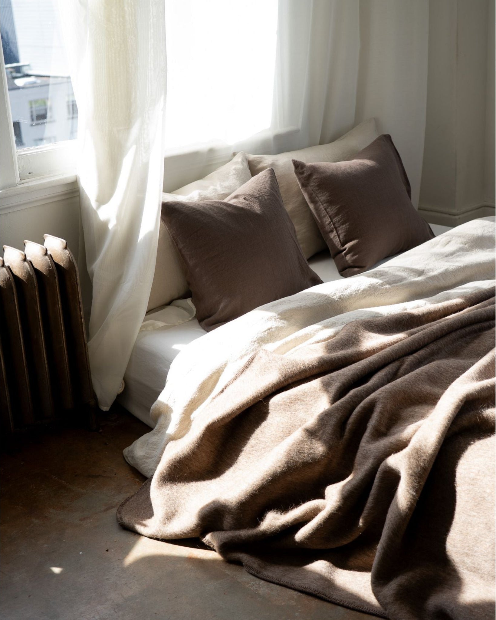 Cozy bedroom with a bed covered in brown blankets and pillows, draped over a window seat.