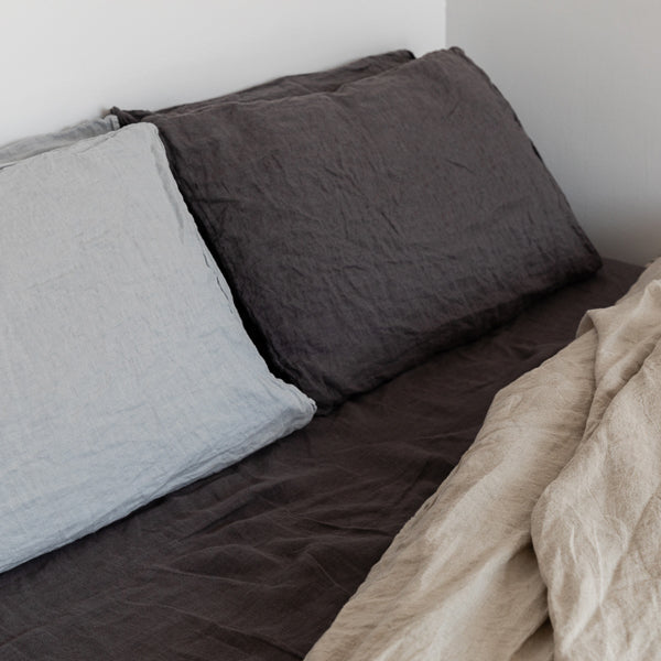 Two pillows on a bed with a beige blanket, against a white wall.