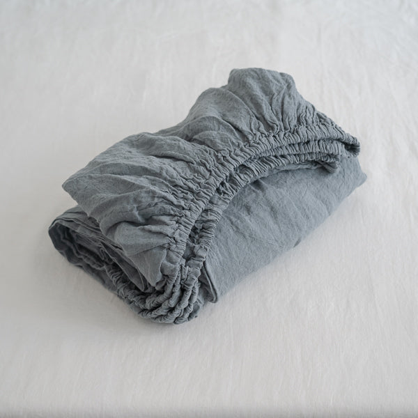 Folded blue fitted sheet on a white bed