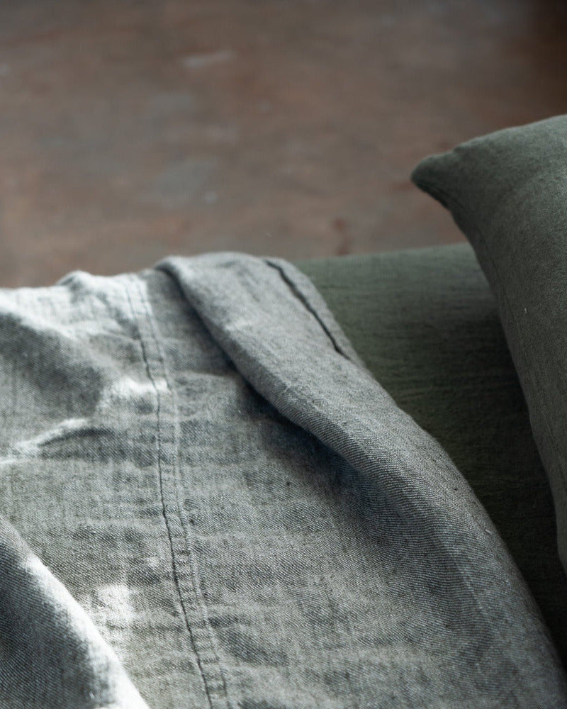 Gray fabric with a textured surface and a green pillow in the background
