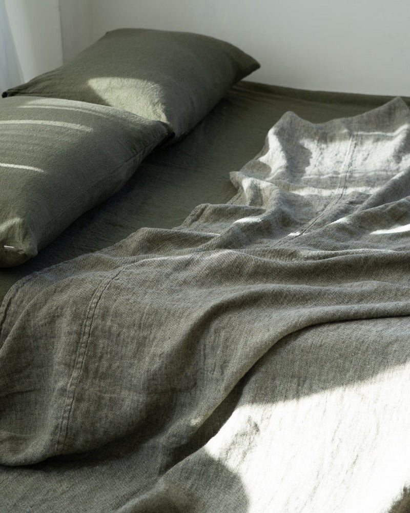 Bed with green bedding and a pillow in a softly lit room