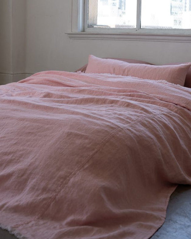 Pink textured bedspread on a bed with pillows in a room with a window.
