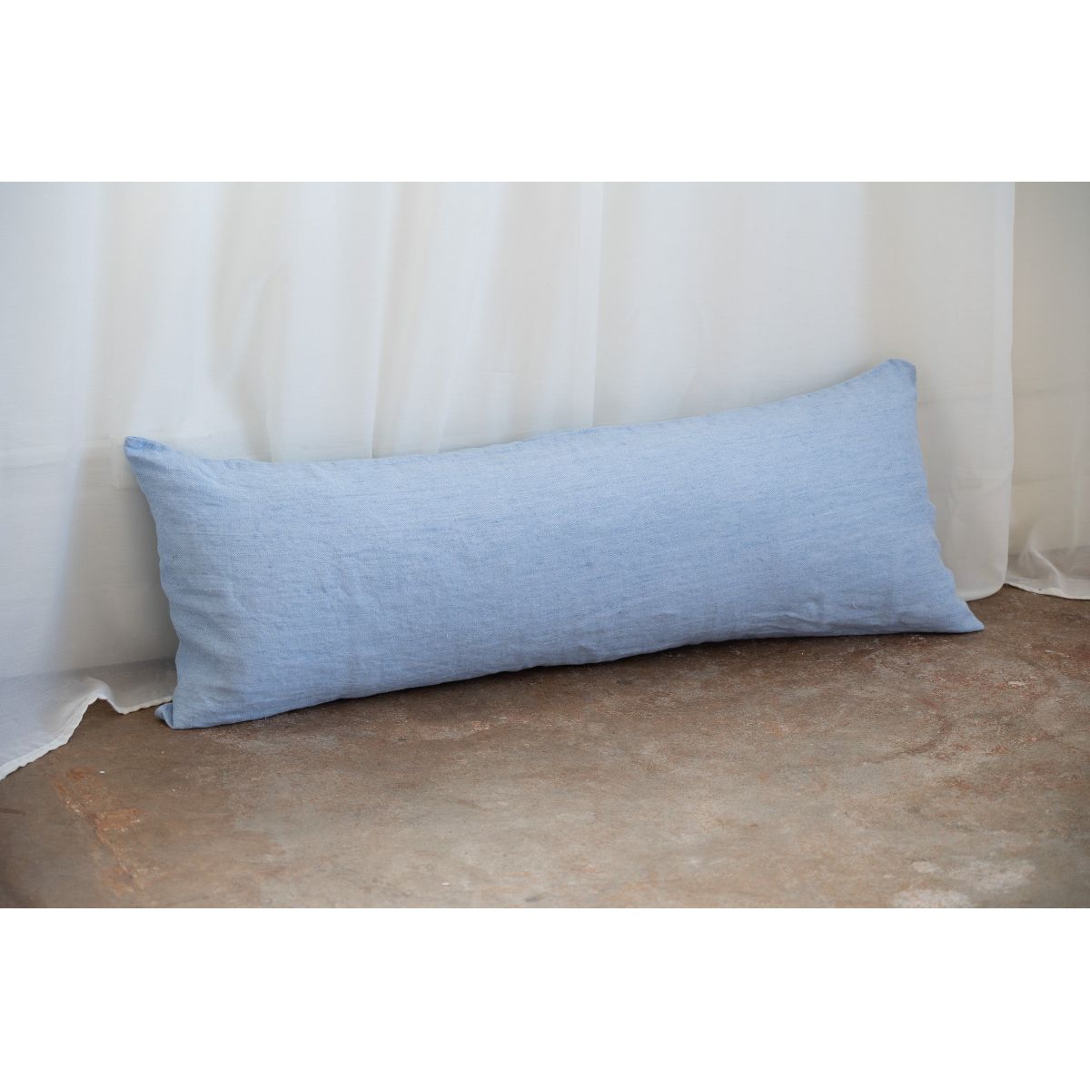 Blue rectangular pillow on a textured surface with a white curtain background