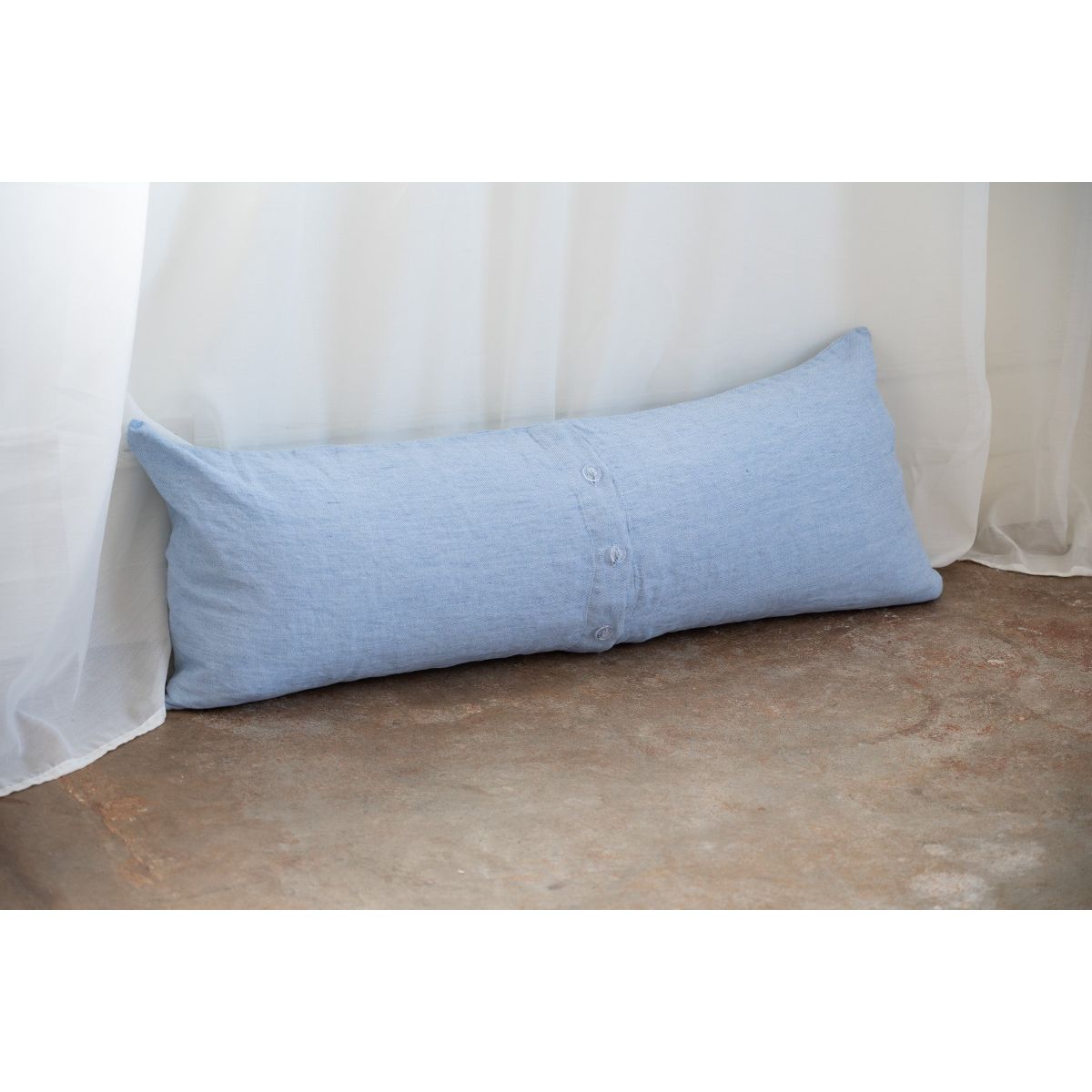 Blue body pillow against a white curtain background