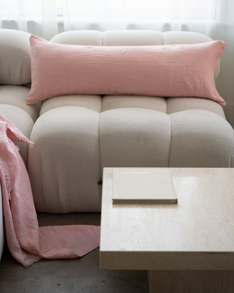 Beige sofa with pink cushions and blanket in a minimalistic room.