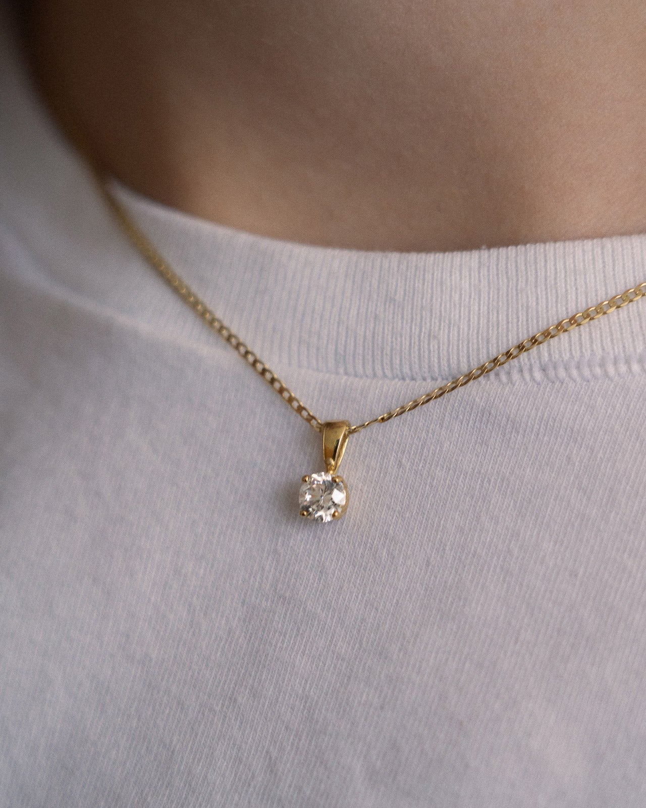 Gold necklace with a diamond pendant on a white shirt
