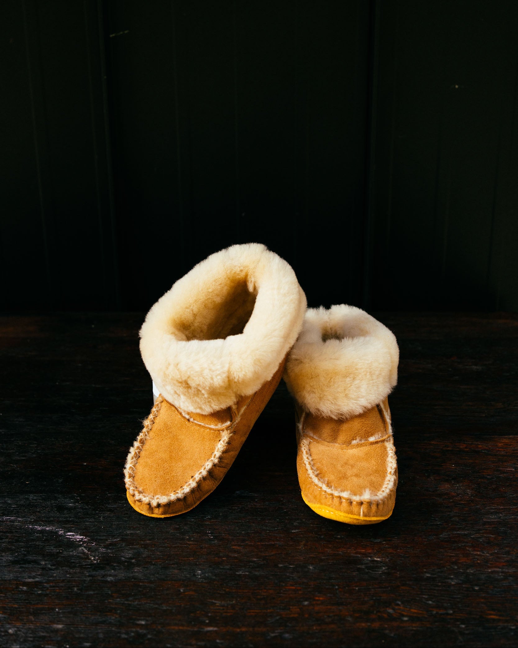 Pair of brown moccasin slippers with white fur lining on a dark wooden surface.