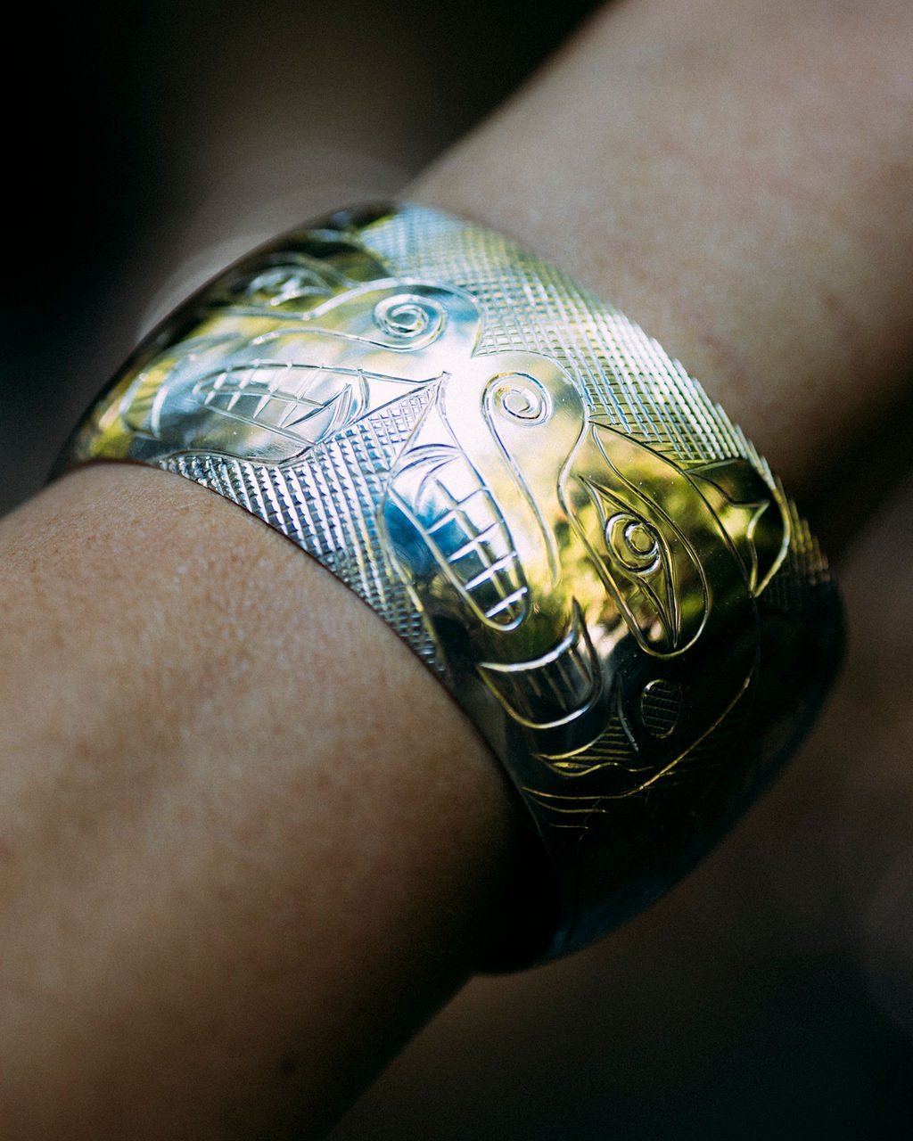 Deb Hunt indigenous carved bears bracelet on a wrist with forest background