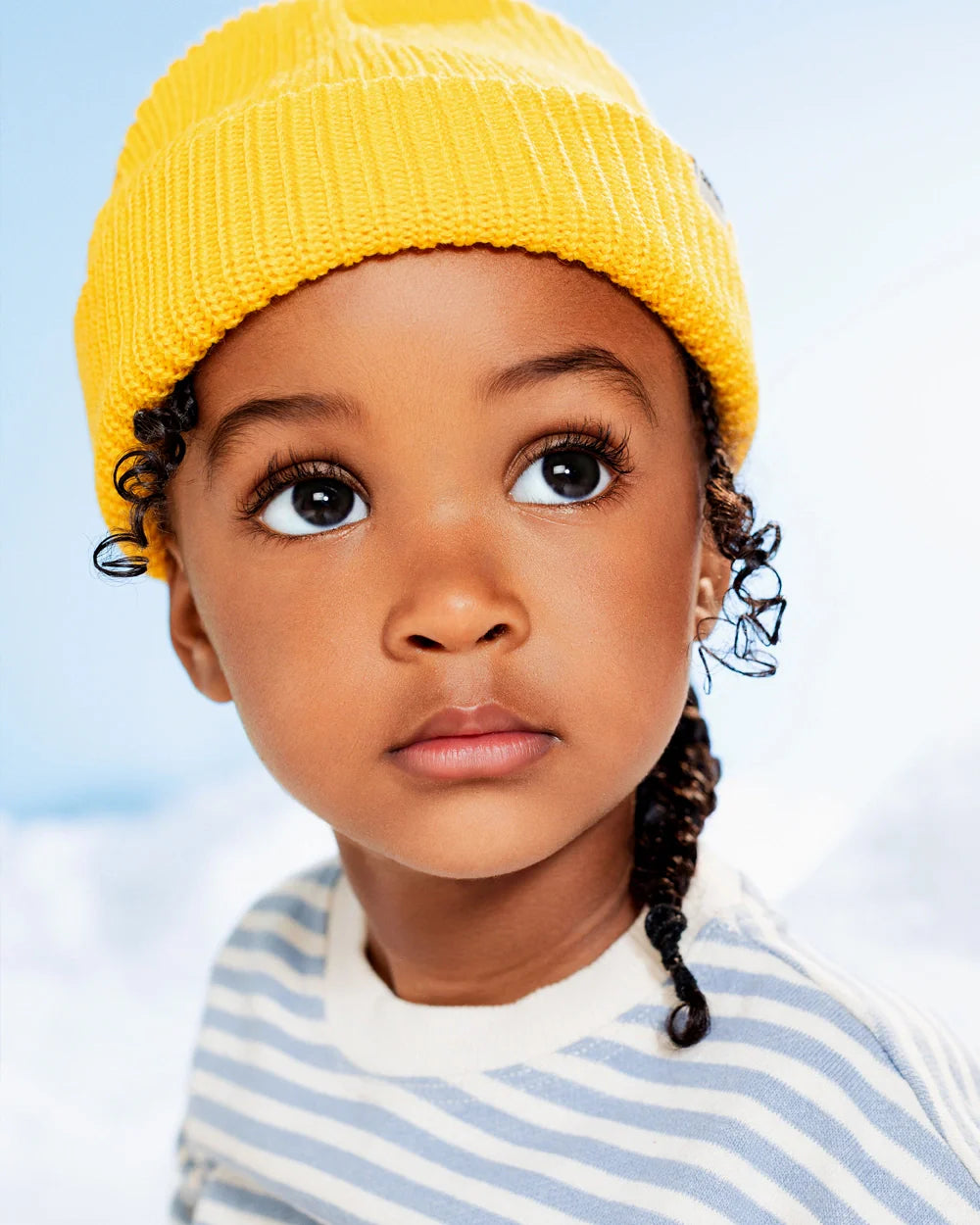 Child wearing a yellow beanie and striped shirt against a blue sky