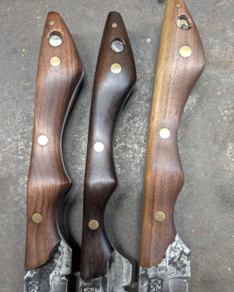 Three handmade sabres with dark wood handles and patterned steel blades, arranged vertically on a textured gray surface.