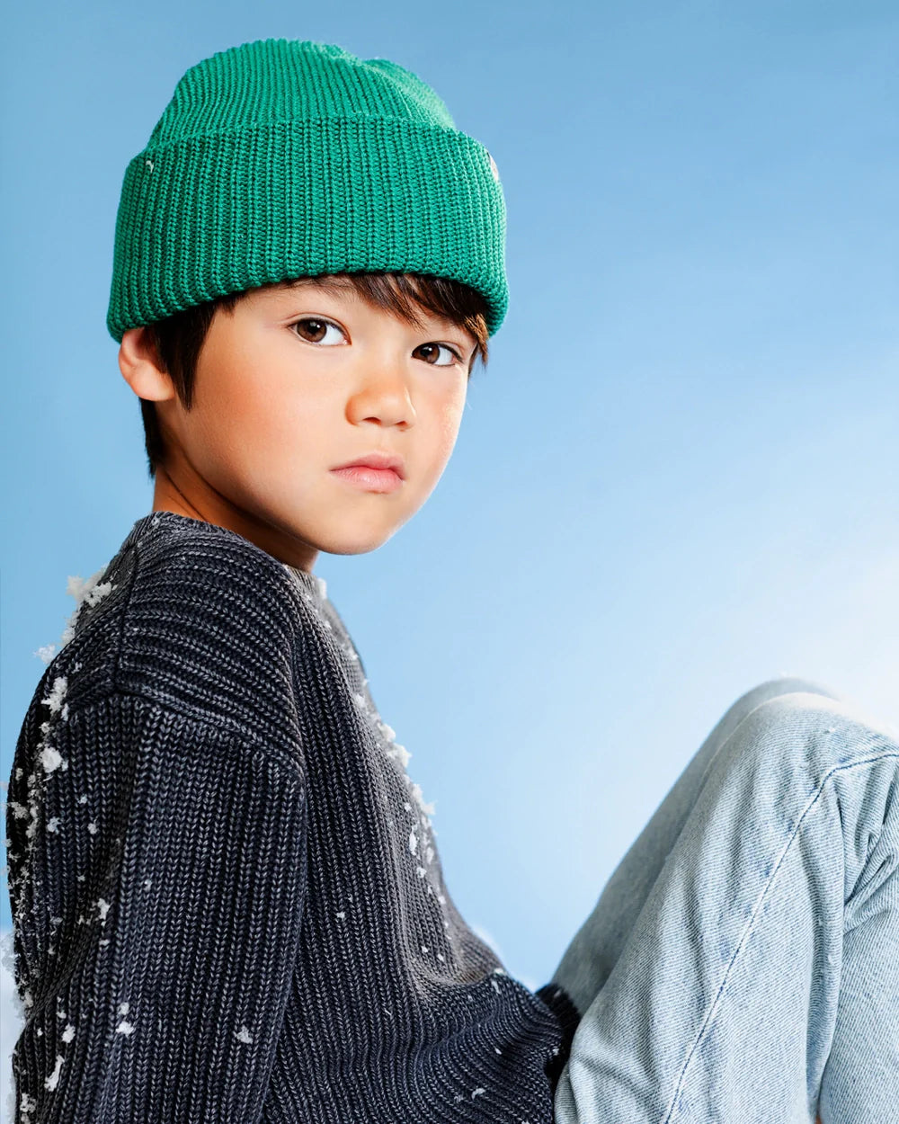 Child wearing a green beanie and gray sweater against a blue background