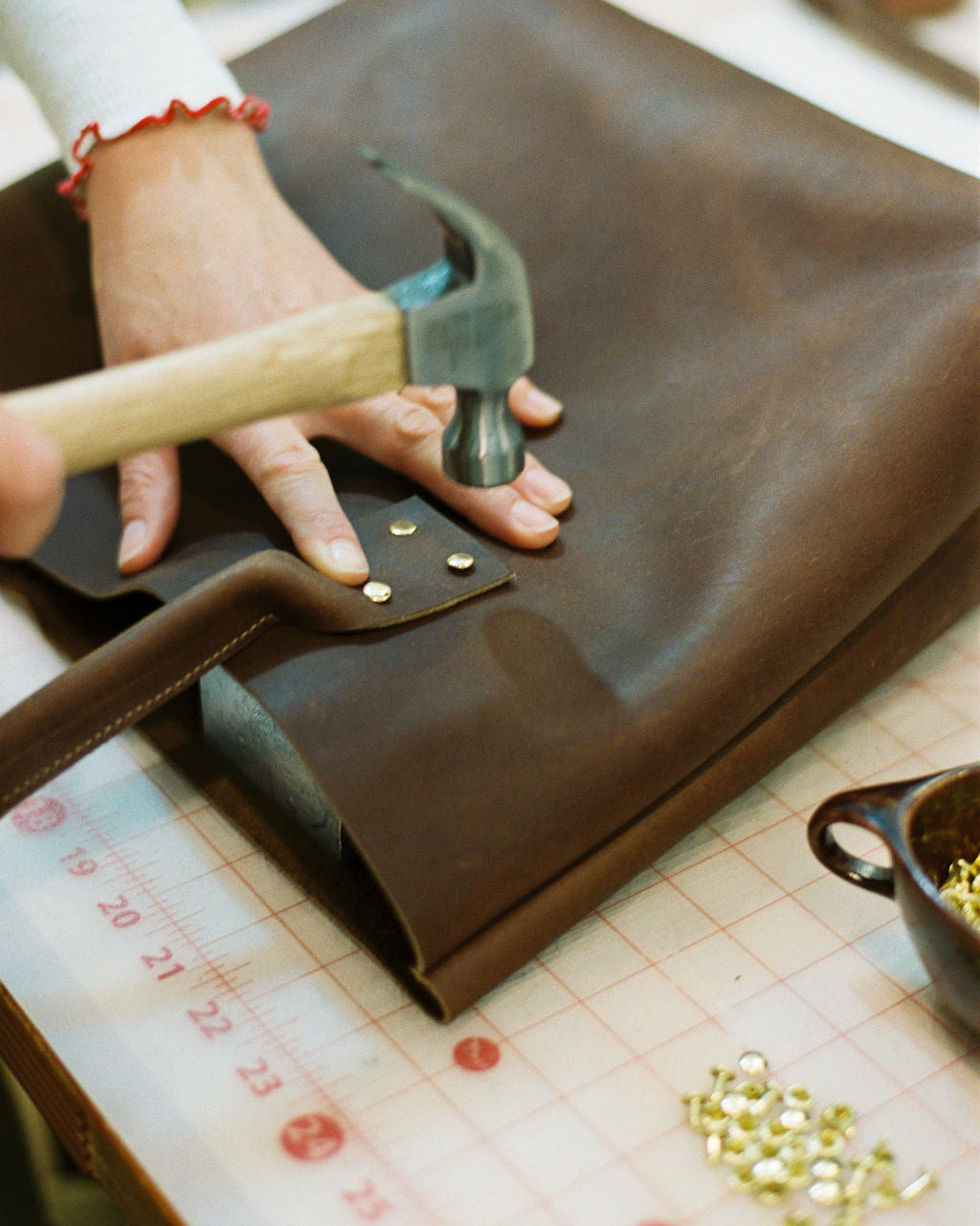 woman making a leather bag, hammering 