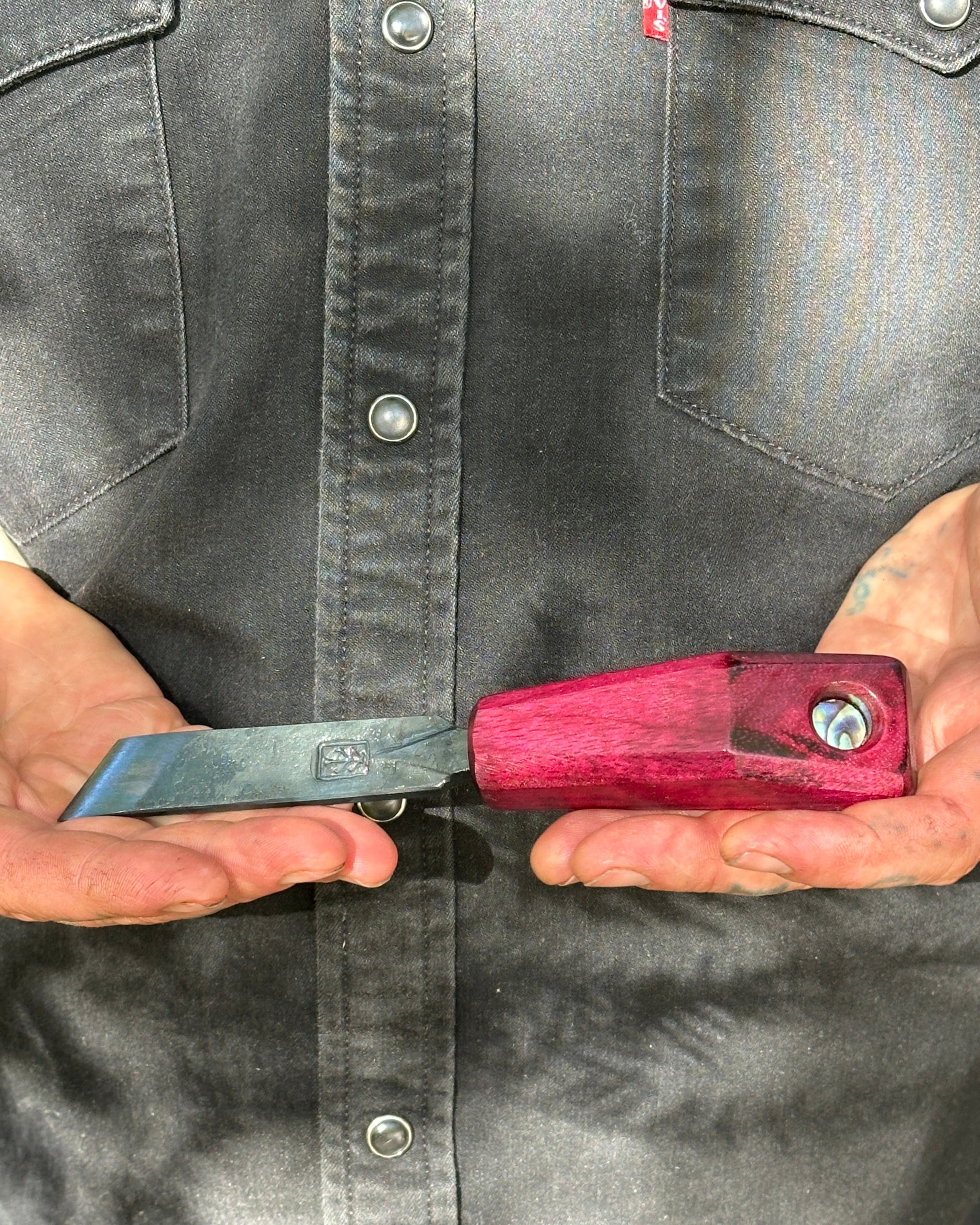 Person holding a shucke with a red handle and black blade against a gray shirt background