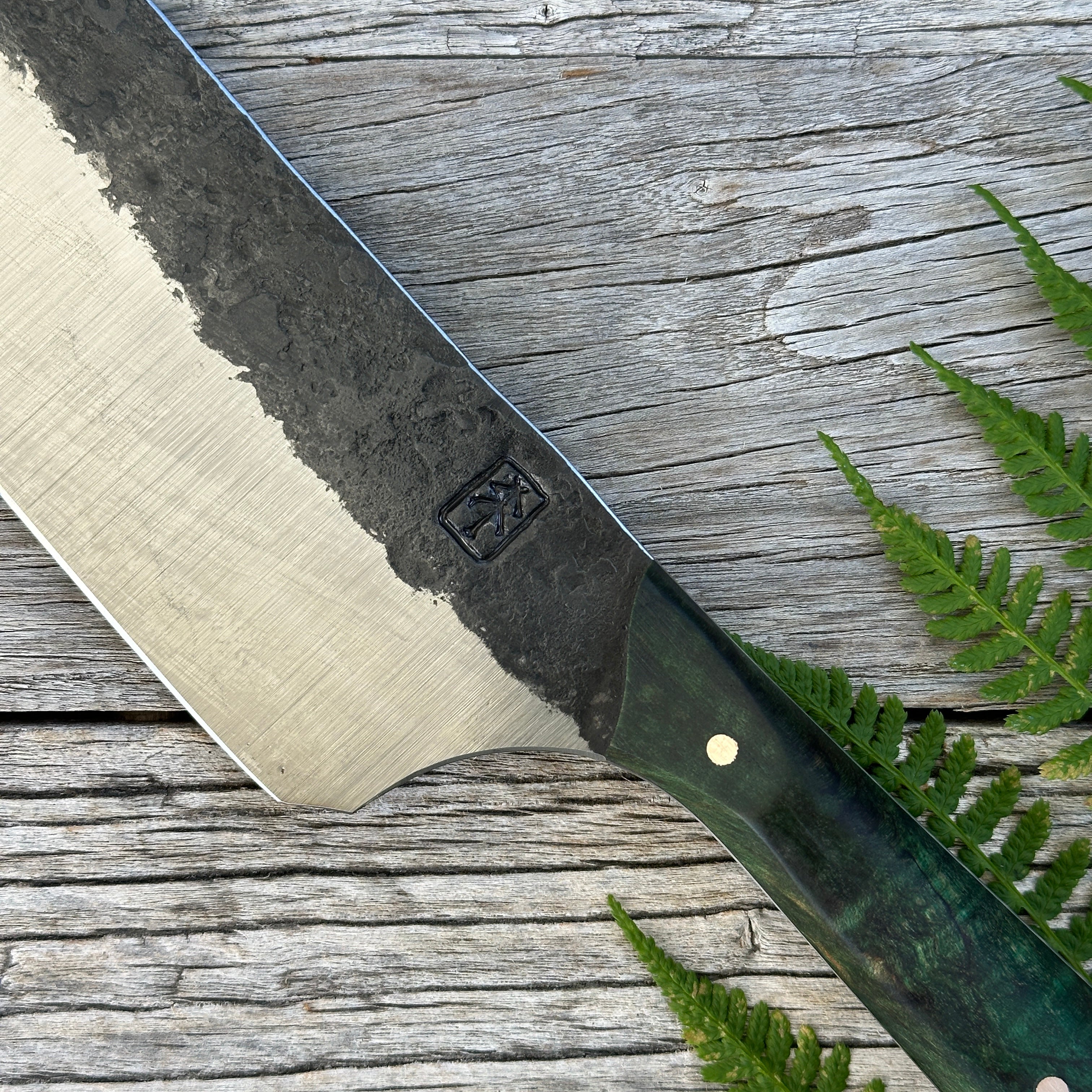 Leechtown Blacksmith Co. for Confluence Nimmo Bay knife blade with a brand logo on a wooden surface with ferns
