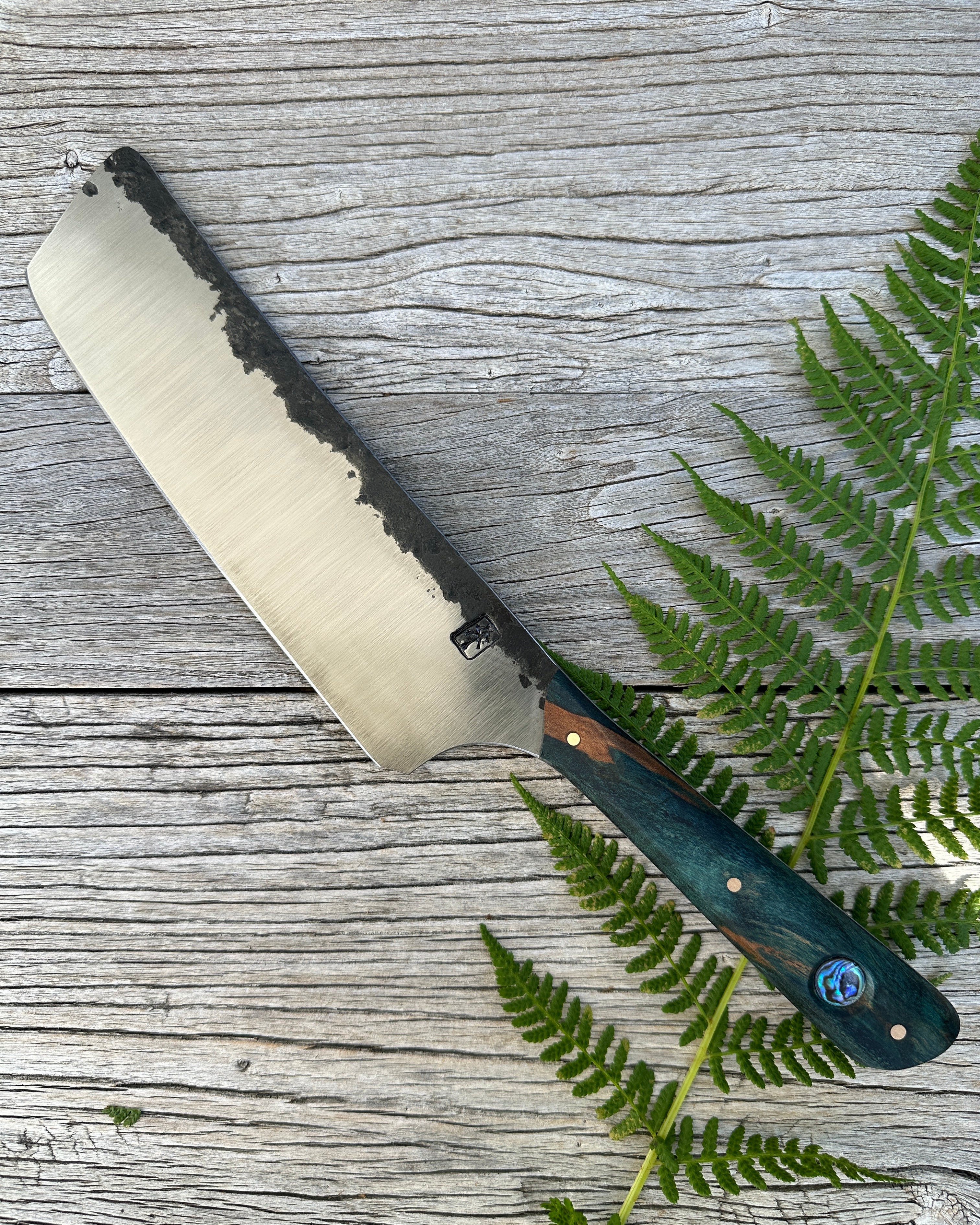 Leechtown Blacksmith Co. for Confluence Nimmo Bay knife with a wooden handle on a wooden surface with fern leaves