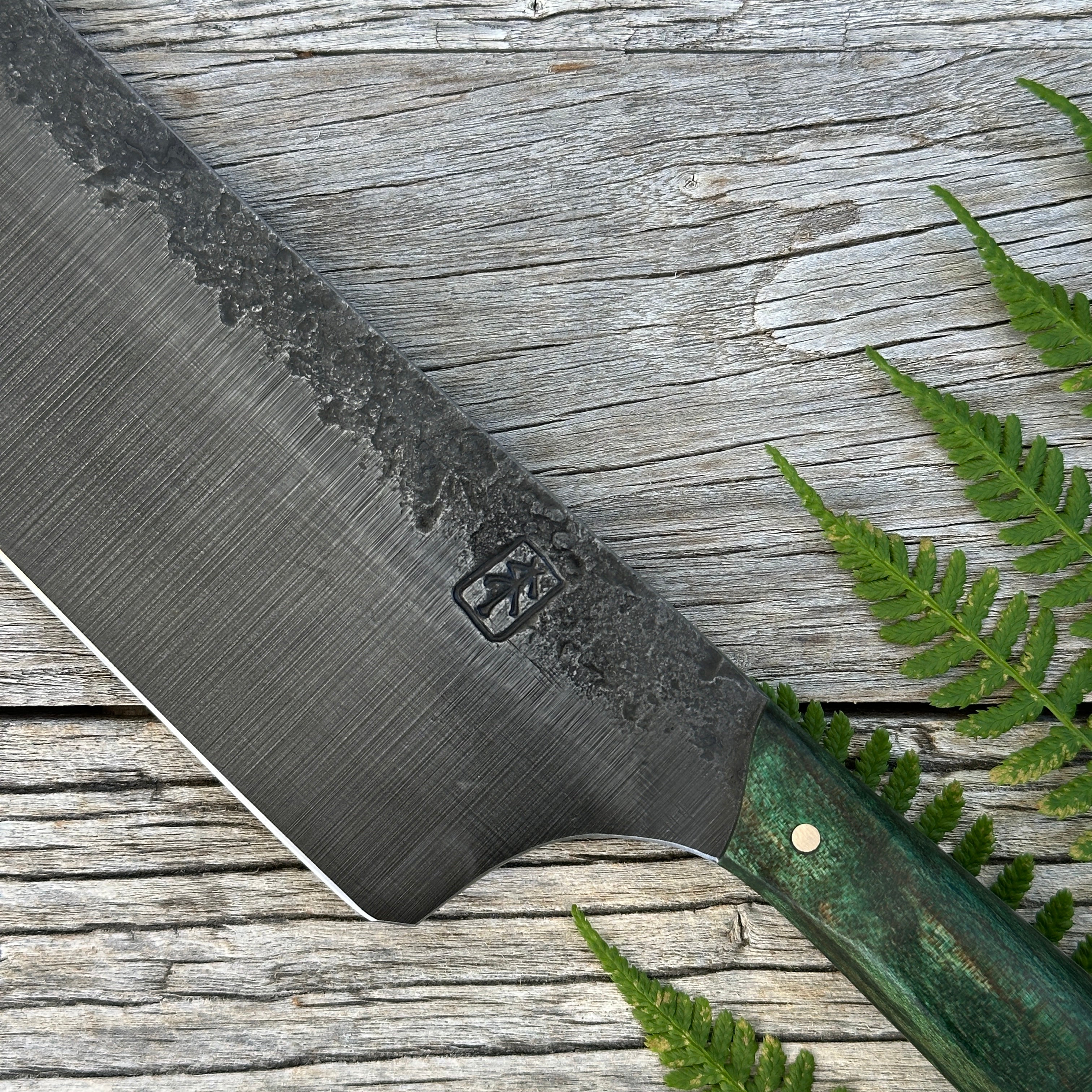 Leechtown Blacksmith Co. for Confluence Nimmo Bay knife blade with a brand logo on a wooden surface with fern leaves