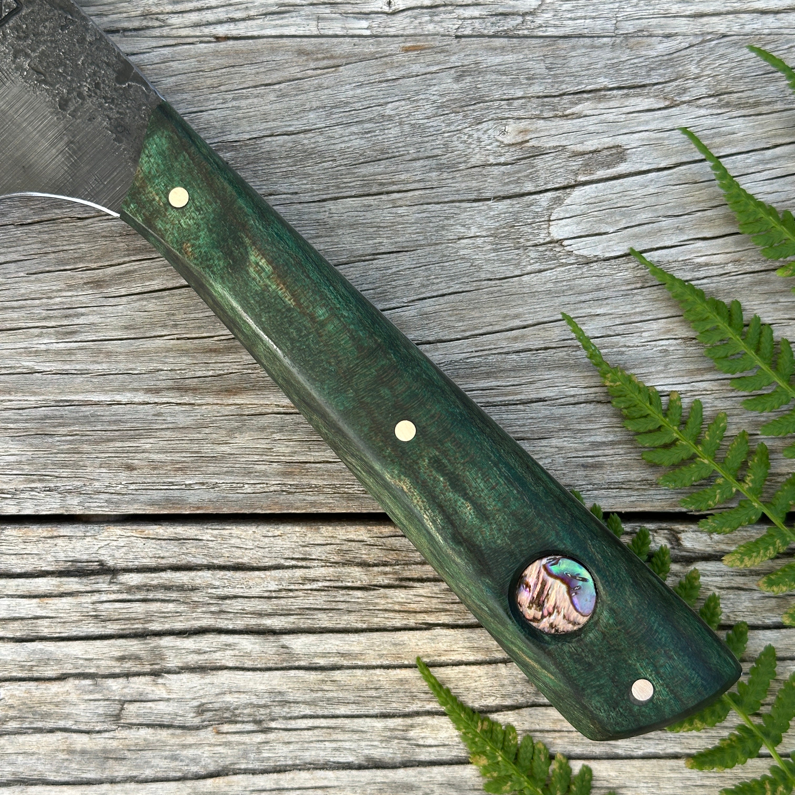 Green-handled Leechtown Blacksmith Co. for Confluence Nimmo Bay knife with a paua inlay on a wooden table with ferns