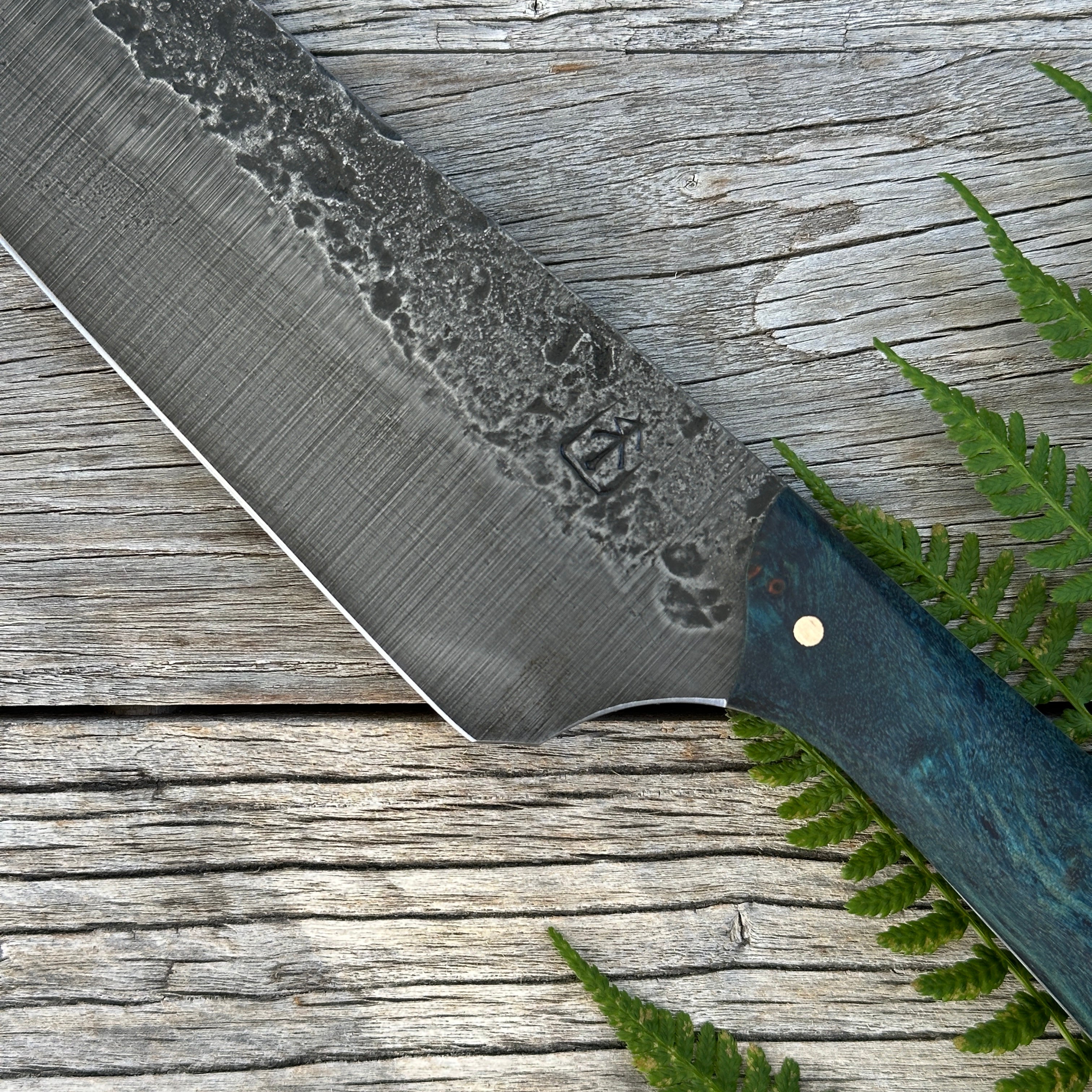 Leechtown Blacksmith Co. for Confluence Nimmo Bay knife with a textured blade on a wooden surface with green leaves