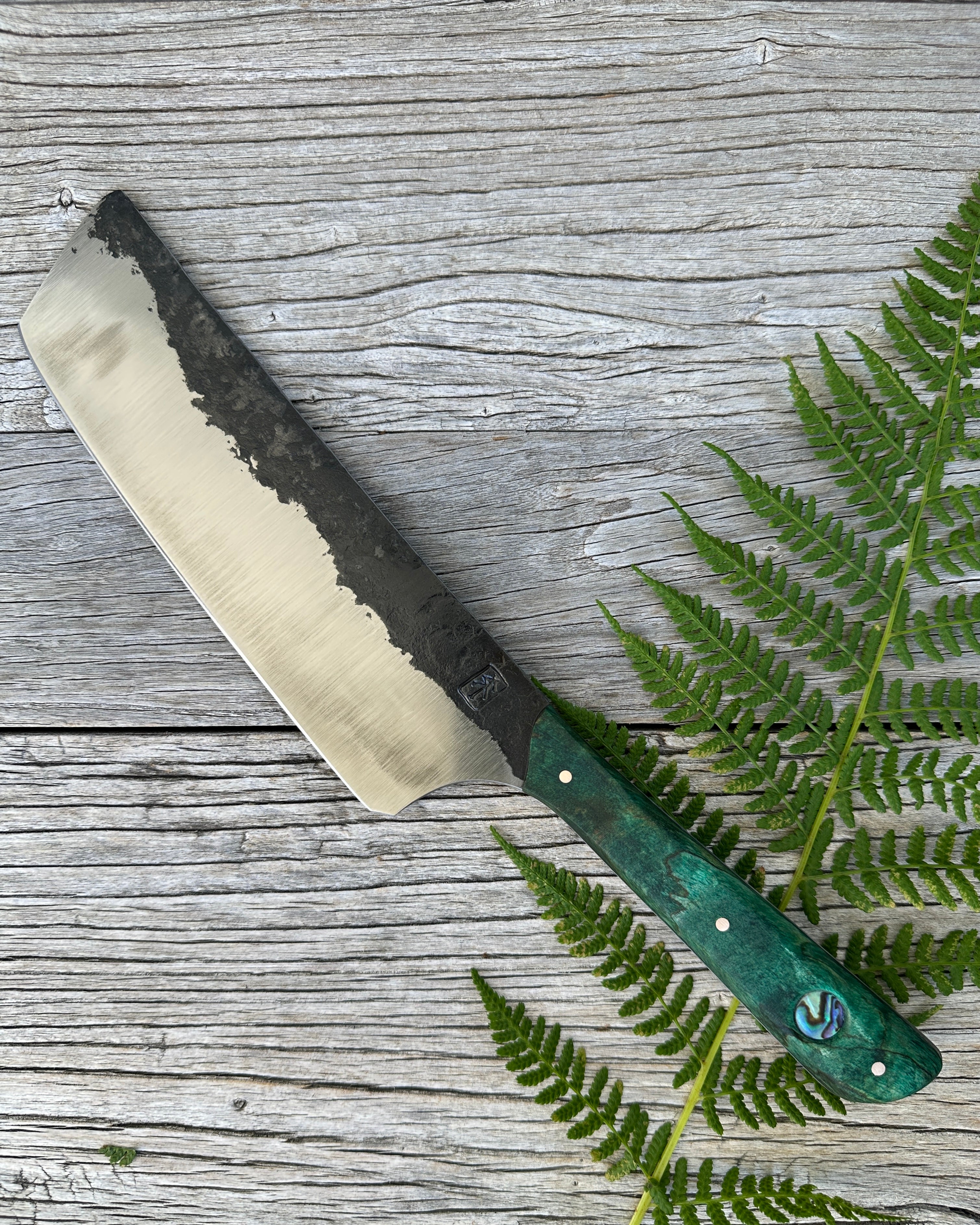 Leechtown Blacksmith Co. knife for Confluence Nimmo Bay with a green handle on a wooden surface with fern leaves