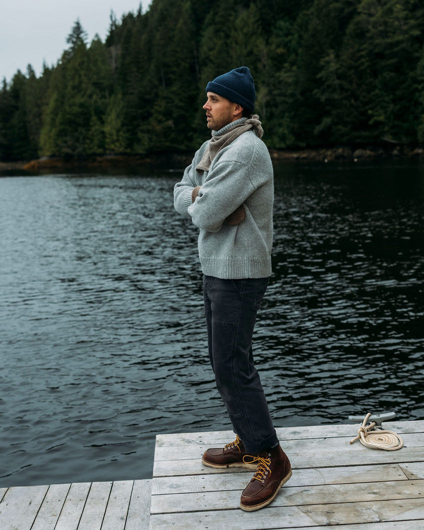 Man standing on a dock wearing a Bare Knitwear turtleneck sweater with ocean and trees in the background
