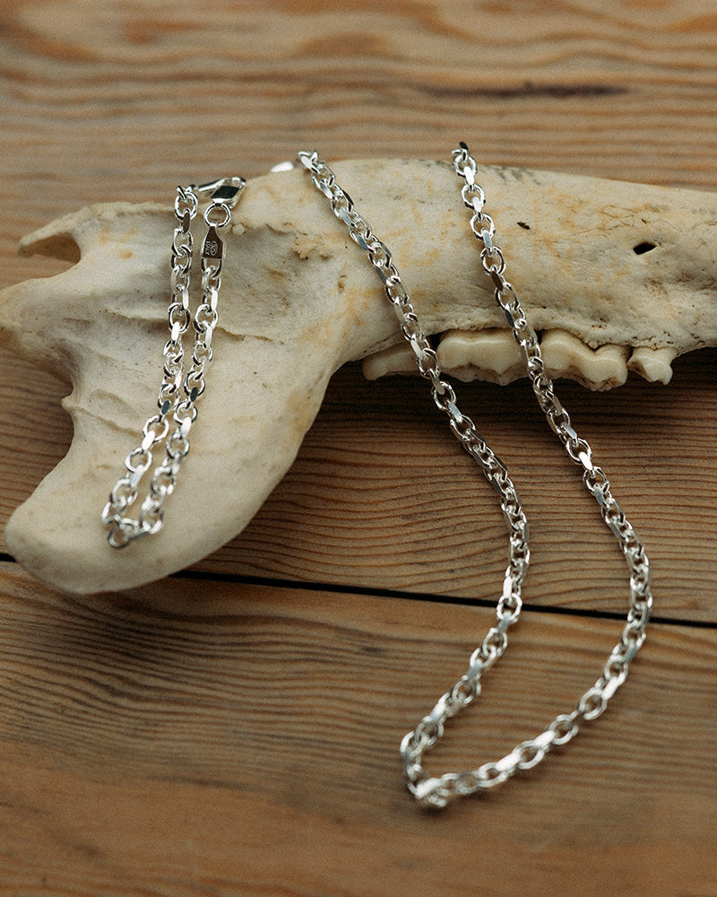 Sow Song Silver chain necklace on a piece of bone with a wooden surface background