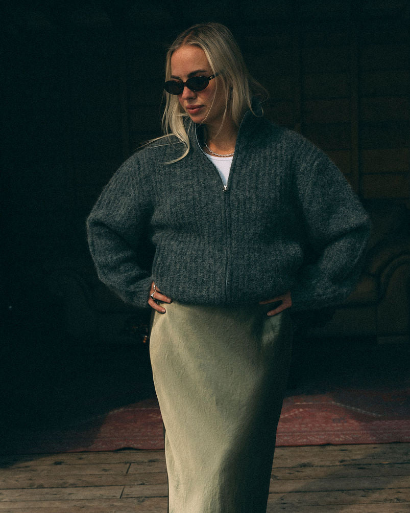 Person wearing a grey Bare Knitwear full zip sweater and skirt against a dark background