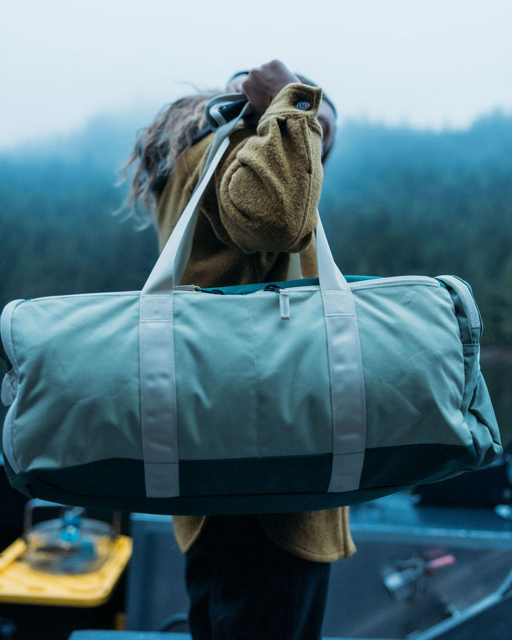 Person holding a green duffel bag with a forest background