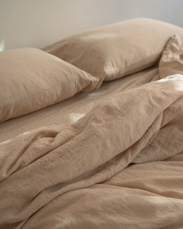 Beige bedding with pillows on a bed in a softly lit room.