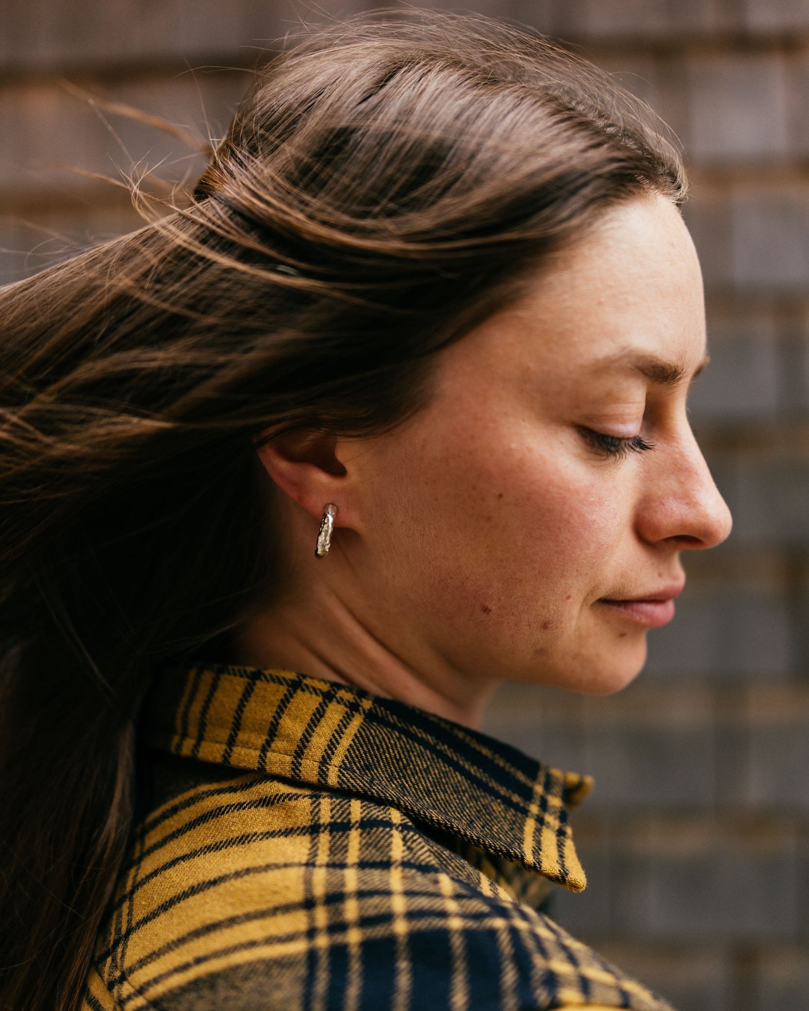 Woman wearing a plaid shirt with a blurred wooden wall background
