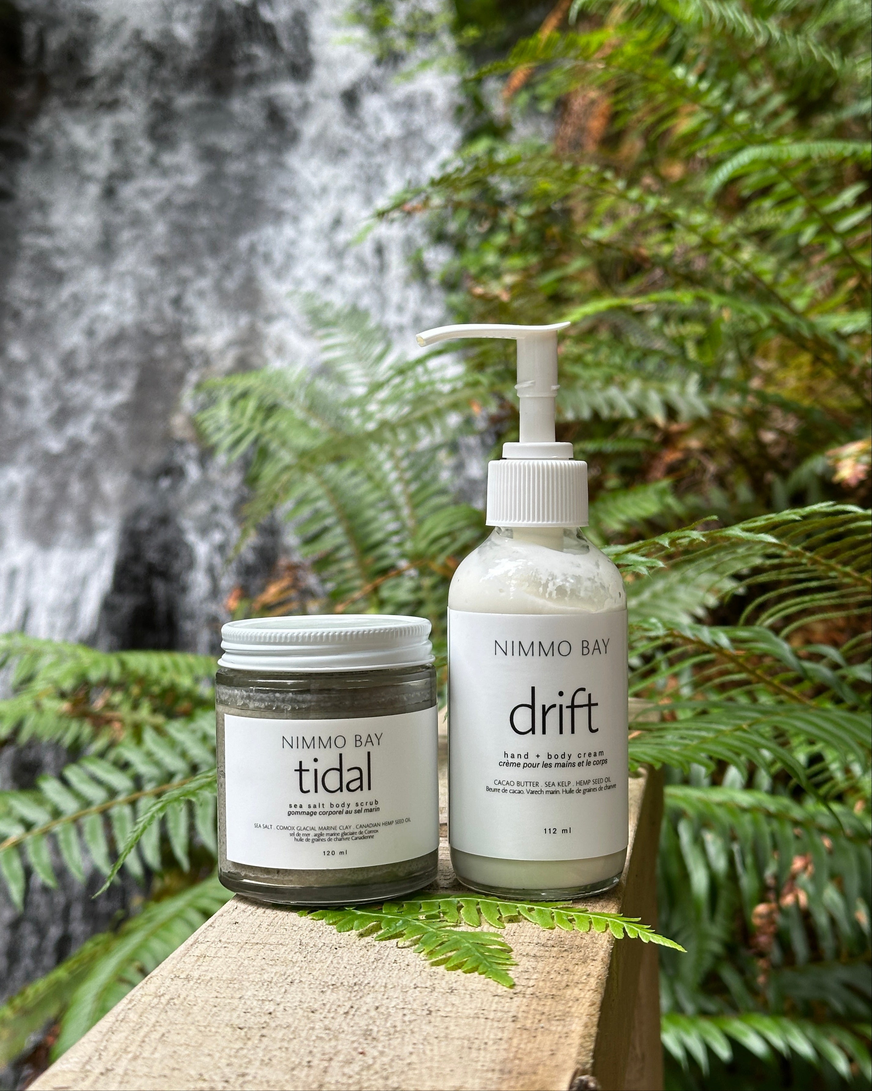 Two bottles of Nimmo Bay products, 'tidal' and 'drift', against a natural background with a waterfall.