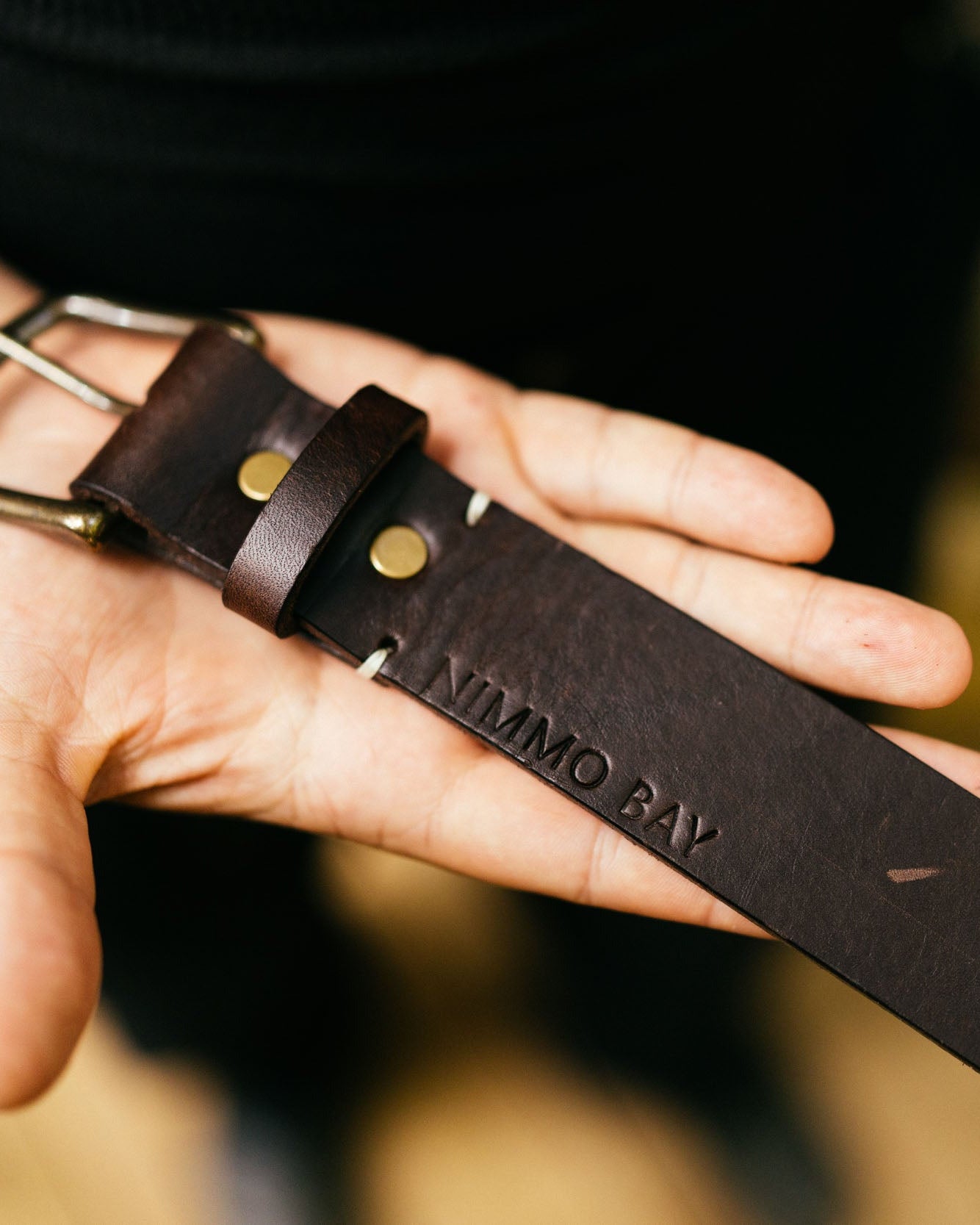 Person holding a brown leather belt with 'Nimmo Bay' branding.