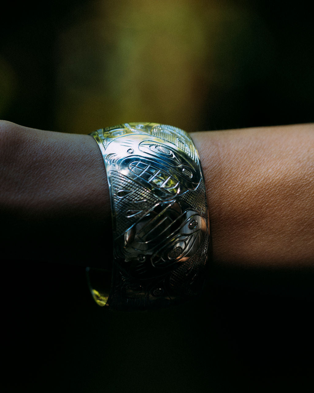 Deb Hunt indigenous carved whales bracelet on a wrist with forest background