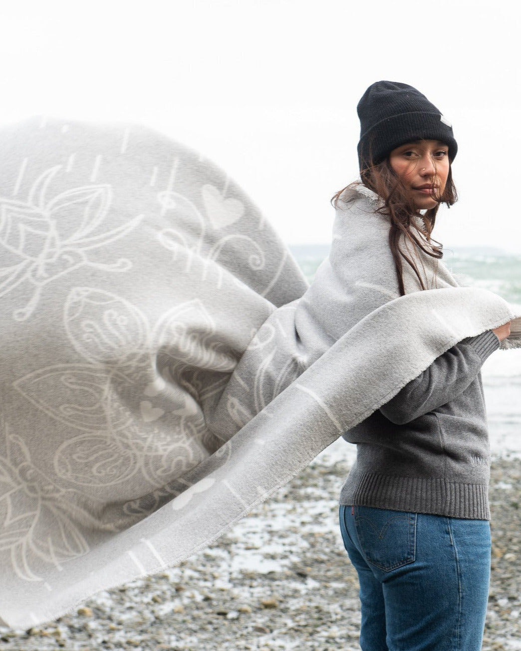 Woman on a beach holding a large birch bark mini tipi everyday blanket with intricate patterns.