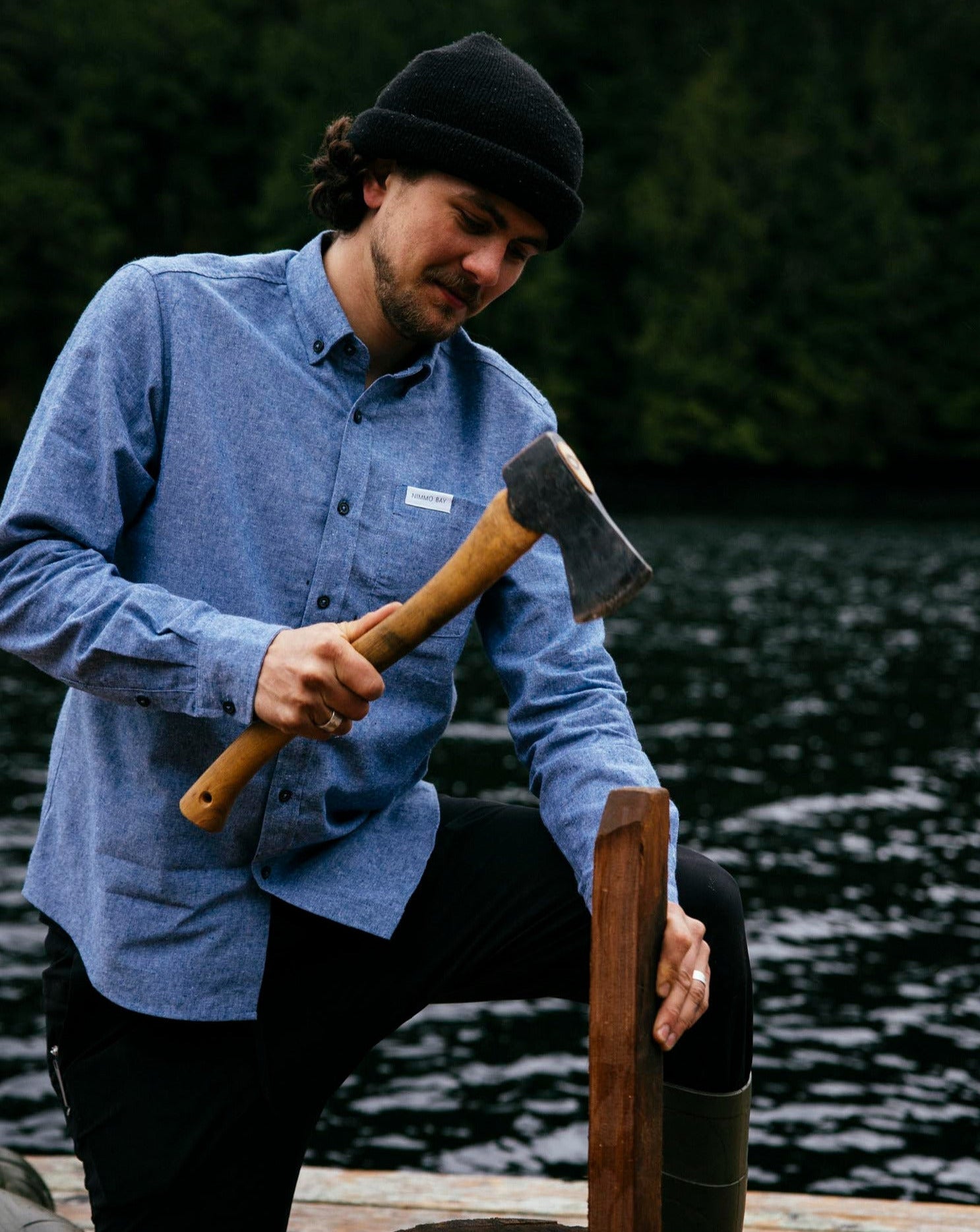 Nimmo Bay x Anian long sleeve blue chambray shirt. Man chopping wood on a dock
