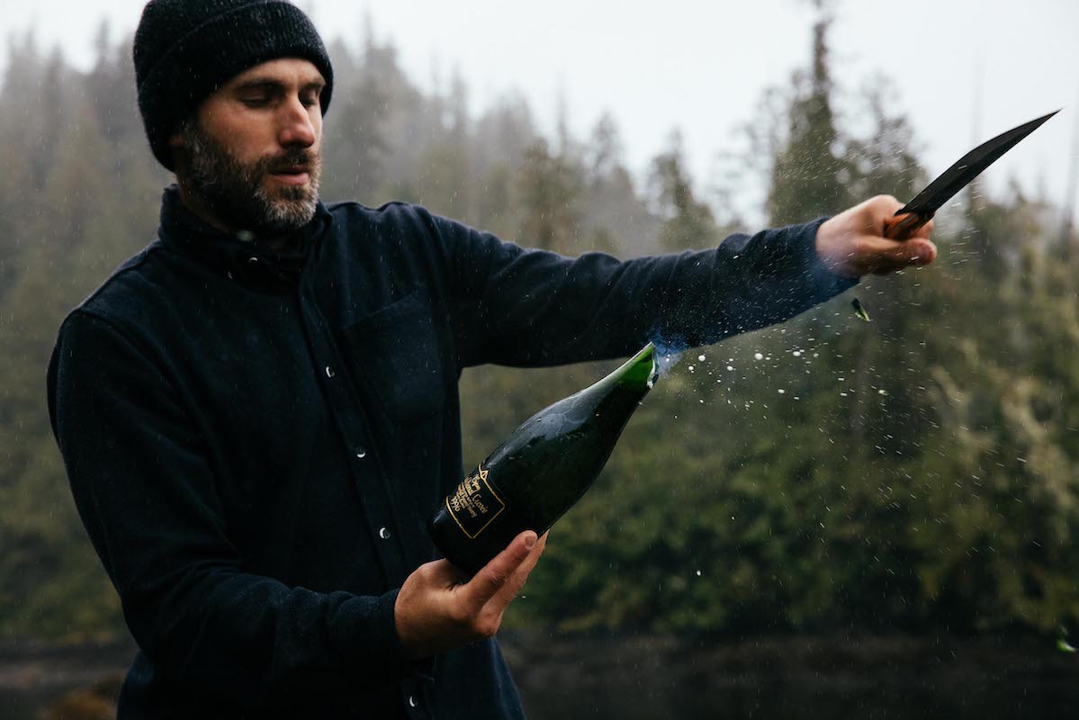 A Man in the rain sabreing with a Leechtown Blacksmith Co. custom champagne sabre with hand-forged steel blade and wooden handle