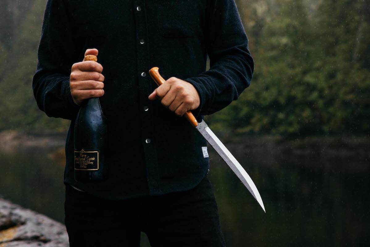 a man in the woods holding a Leechtown Blacksmith Co. custom champagne sabre with hand-forged steel blade and wooden handle